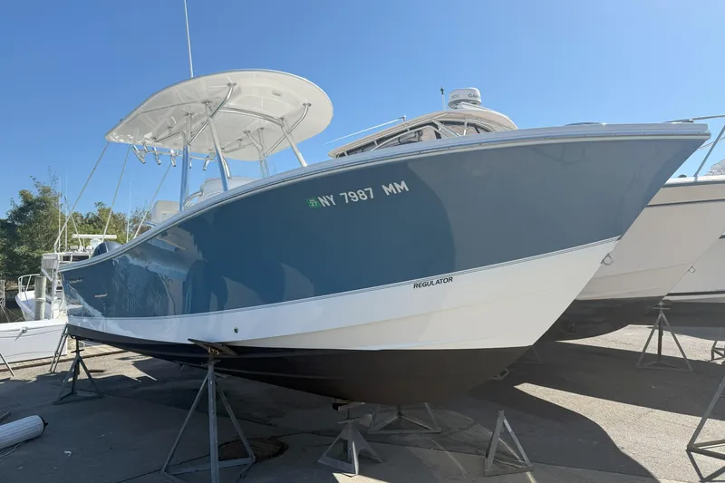 Slide: The Image of 2017 Regulator 25 boat on stands, blue hull, sunny day. - 3