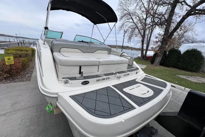 Slide: The Image of 2010 Sea Ray 220 Sundeck boat docked near a lake, showcasing rear seating and swim platform. - 8