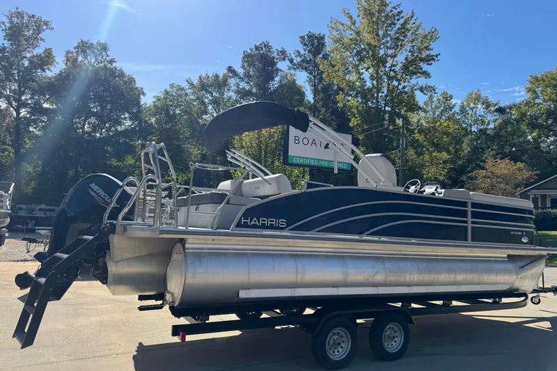 Slide: The Image of 2025 Harris Sunliner 230 pontoon boat on trailer, parked outdoors under clear blue sky. - 2