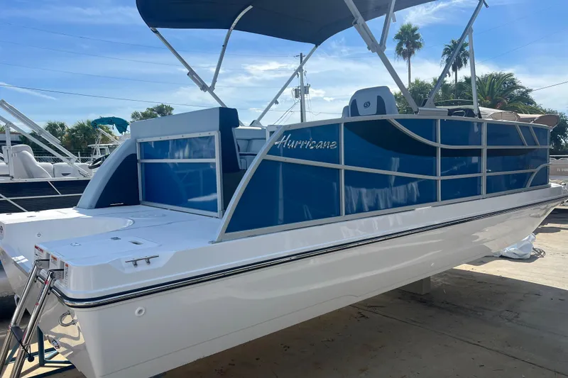 Slide: The Image of 2025 Hurricane FunDeck 2260 RE OB boat with blue and white design, docked under clear sky. - 0