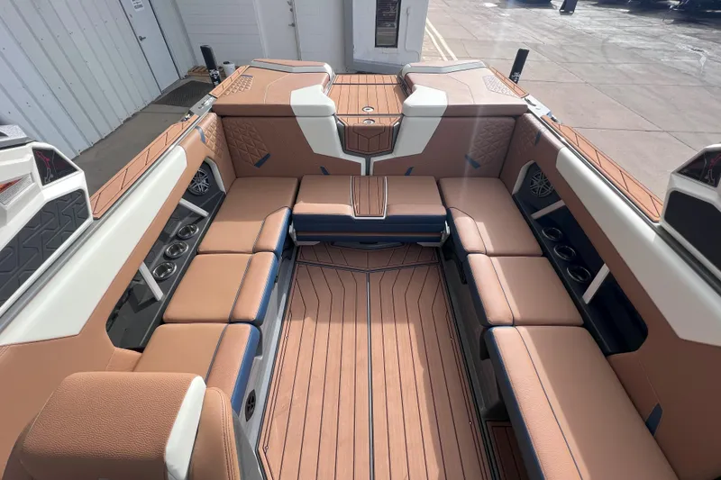 Slide: The Image of 2024 Nautique Super Air Nautique GS22 interior with tan and blue seating, cup holders, and speakers. - 13