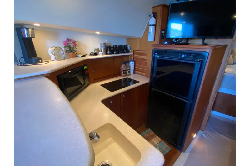 Slide: The Image of 2002 Silverton 330 Sport Bridge kitchen with appliances, sink, and TV in cozy cabin setting. - 25