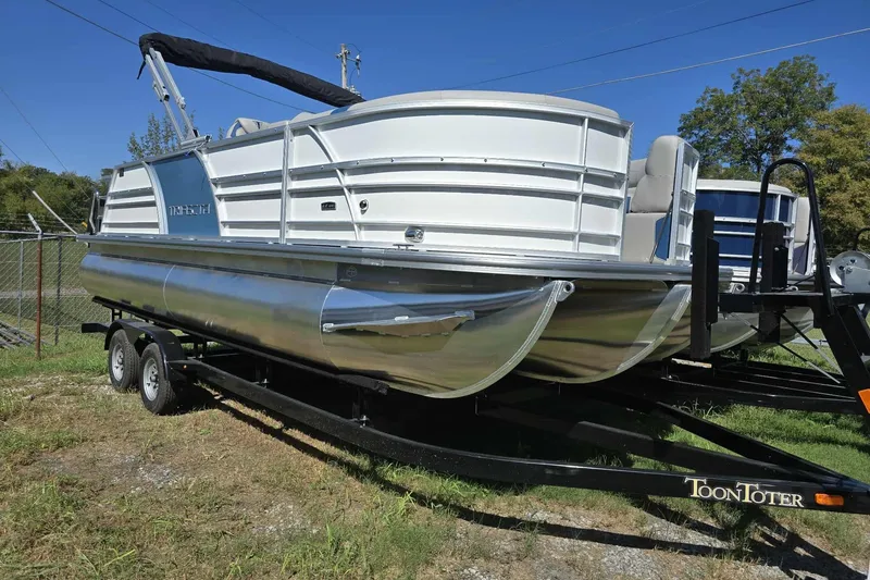 The Image of 2026 Trifecta 25LE pontoon boat on trailer, parked outdoors under clear blue sky. - 1