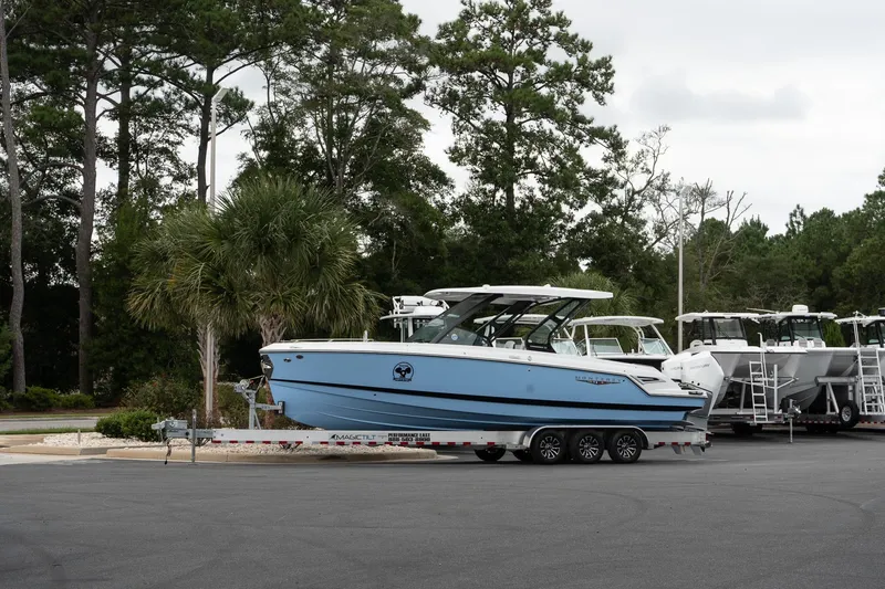 Slide: The Image of 2026 Monterey Elite 30 OB boat on trailer, parked near trees and other boats. - 13