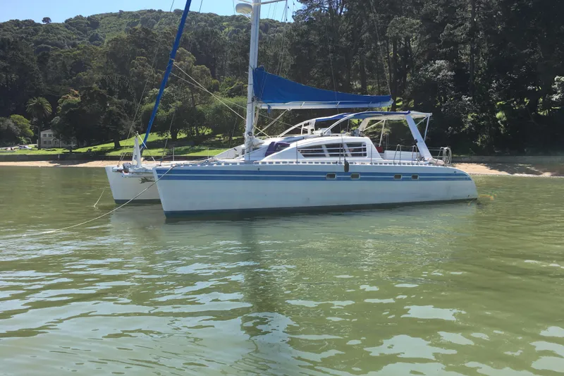 Slide: The Image of 1992 Wauquiez Kronos catamaran anchored near a lush, forested shoreline. - 2