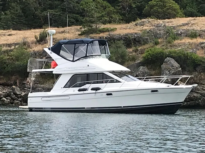 The Image of 1999 Bayliner 3388 Motoryacht anchored near rocky shoreline. - 0