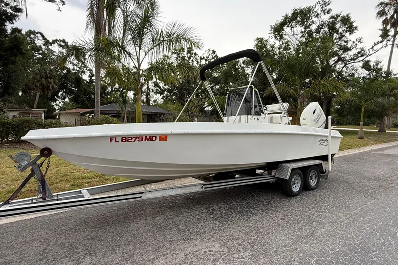 Slide: The Image of 2002 Spectre 22CC boat on trailer, parked roadside with palm trees in background. - 2