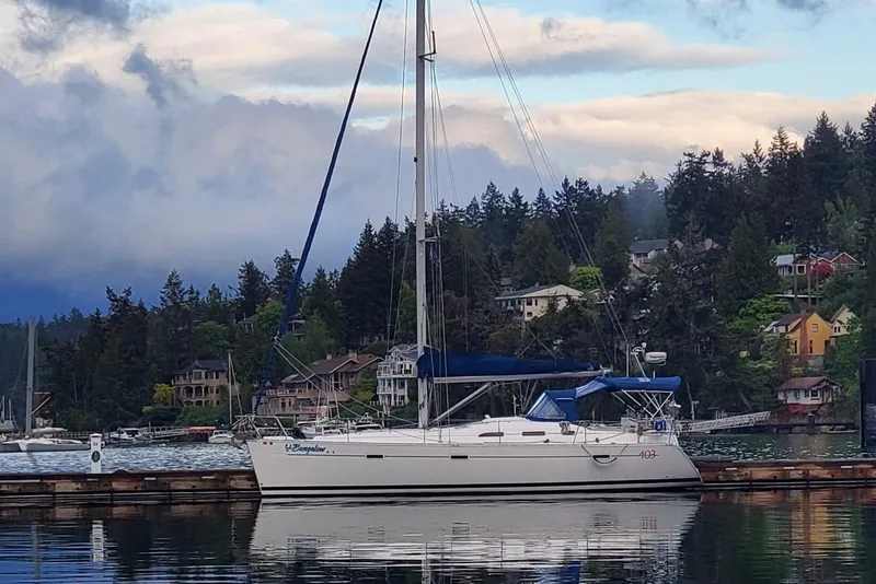 The Image of 2006 Beneteau Oceanis 393 sailboat docked in a scenic harbor with forested hills. - 0