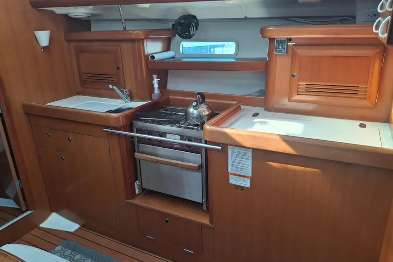Slide: The Image of 2006 Beneteau Oceanis 393 yacht kitchen with stove, sink, and wooden cabinetry. - 21