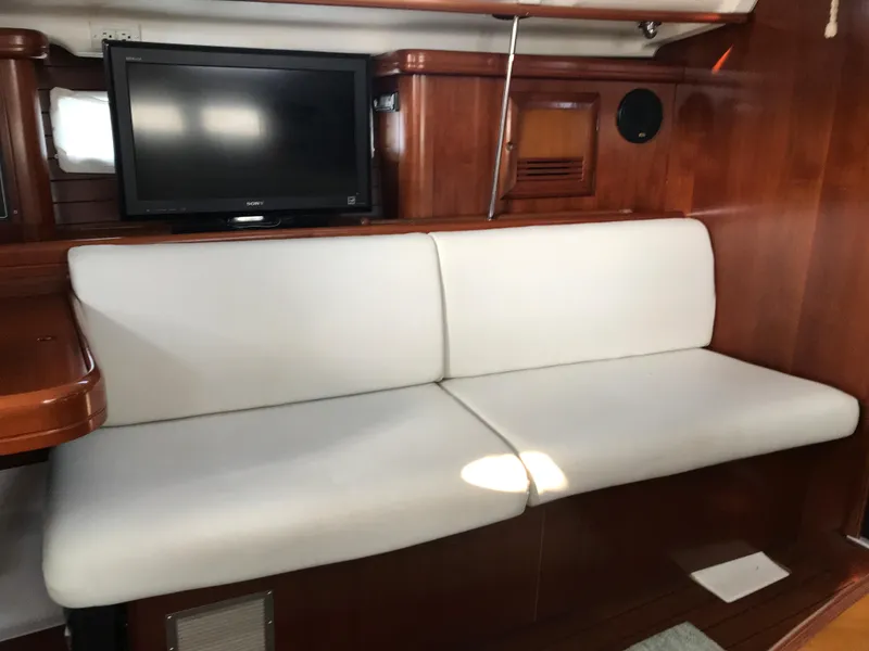 Slide: The Image of White cushioned seating in 2003 Beneteau 411 yacht interior with wooden paneling and mounted TV. - 6