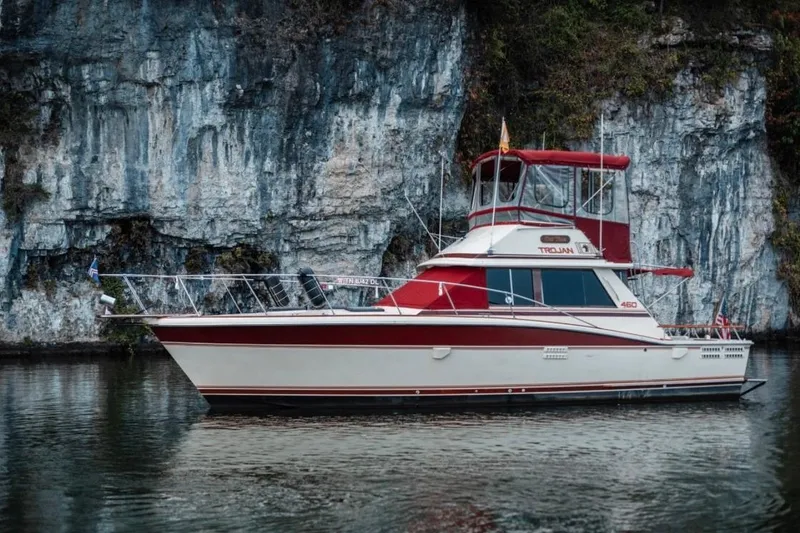 The Image of 1982 Trojan F-36 Convertible yacht on calm water near rocky cliffs. - 0