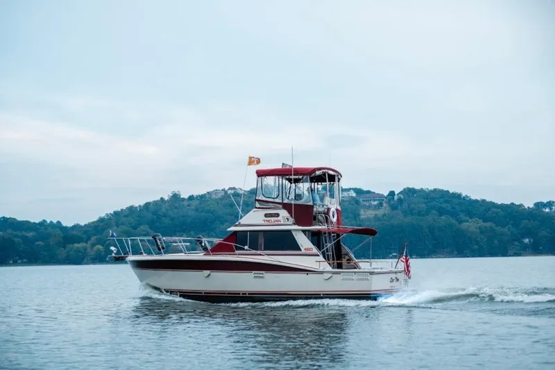 Slide: The Image of 1982 Trojan F-36 Convertible boat cruising on a serene lake with forested hills. - 28