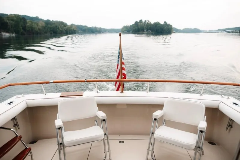 Slide: The Image of 1982 Trojan F-36 Convertible boat deck with chairs, American flag, and scenic water view. - 3