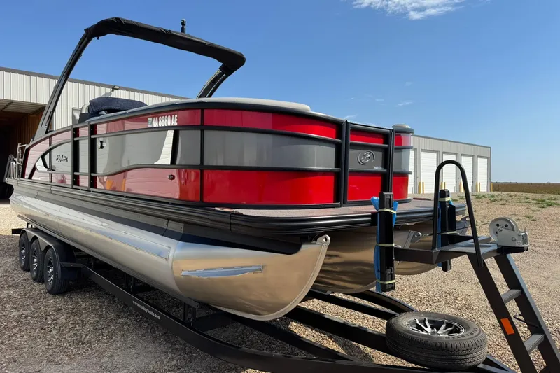 Slide: The Image of 2025 Barletta LUSSO 25UCAT pontoon boat on trailer, red and black design, parked outdoors. - 16