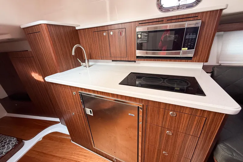 Slide: The Image of 2016 Pursuit OS 355 Offshore yacht kitchen with wood cabinetry, sink, microwave, and stovetop. - 36