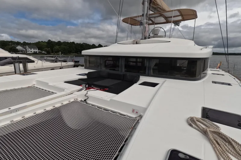 Slide: The Image of 2021 Lagoon 51 catamaran with spacious deck and netting, docked by a scenic shoreline. - 13