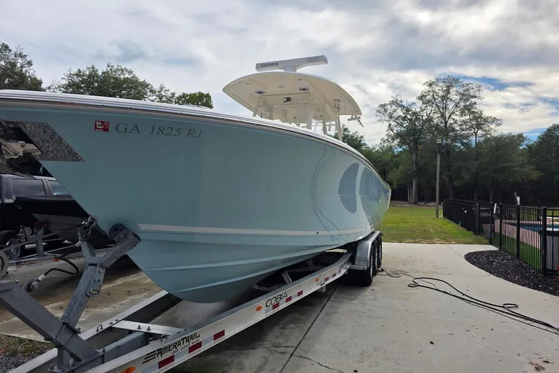 Slide: The Image of 2022 Cobia 320 Center Console boat on trailer, parked outdoors with trees in background. - 2