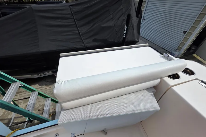 Slide: The Image of 2022 Cobia 320 Center Console boat seat and storage area, docked near a garage. - 27