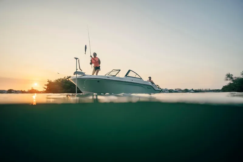 Slide: The Image of 2026 Bayliner Trophy T22SC boat at sunset, with people fishing on calm water. - 33