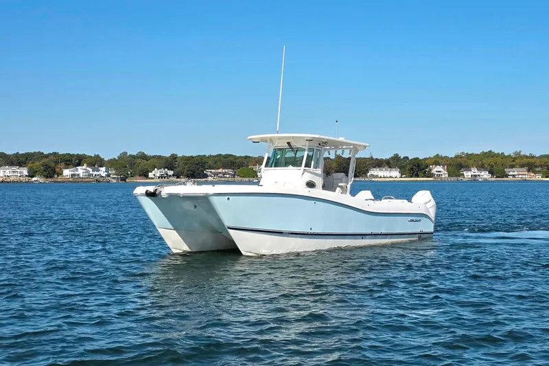 Slide: The Image of 2024 World Cat 325 CC boat cruising on a calm lake with houses in the background. - 21