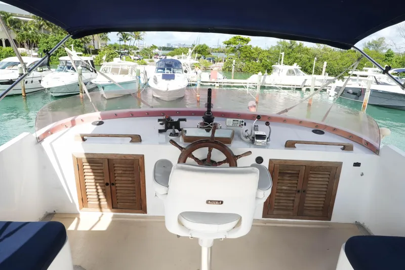 Slide: The Image of 1982 CHB Classic Trawler 41 helm with wooden wheel, marina view, and surrounding boats. - 10