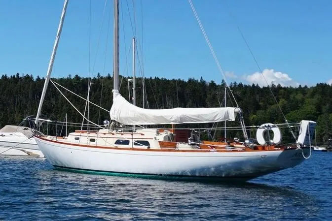The Image of 1970 Hinckley Pilot 35 sailboat anchored on a calm lake with forested background. - 0