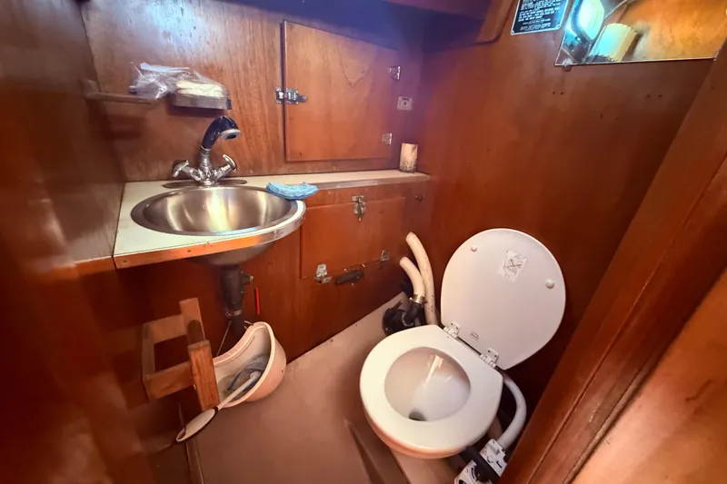Slide: The Image of 1970 Hinckley Pilot 35 yacht bathroom with sink and toilet, featuring wooden cabinetry. - 11