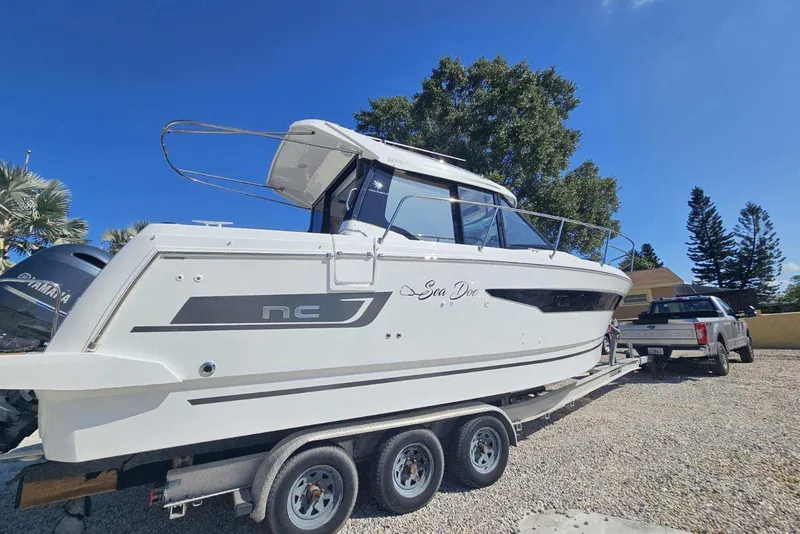 Slide: The Image of 2024 Jeanneau NC Weekender 895 boat on trailer, parked outdoors under clear blue sky. - 2