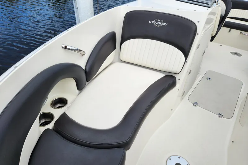 Slide: The Image of 2017 Stingray 214 LR boat interior with black and white seating, cup holders, and water view. - 17