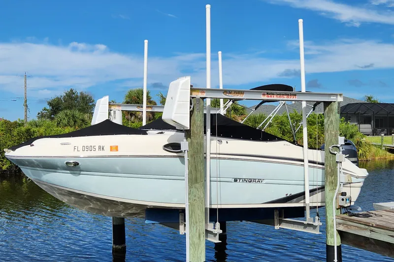 Slide: The Image of 2017 Stingray 214 LR boat on lift, docked by lush greenery under clear blue sky. - 28