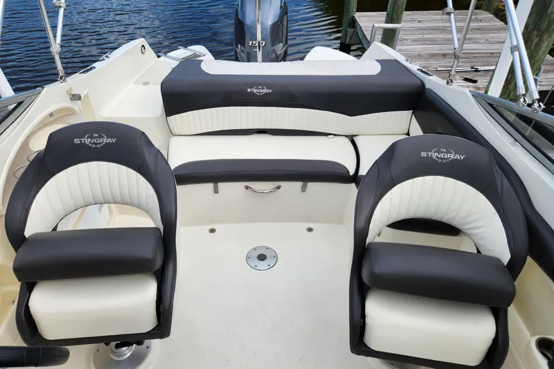 Slide: The Image of 2017 Stingray 214 LR boat interior with black and white seating, docked by water. - 8