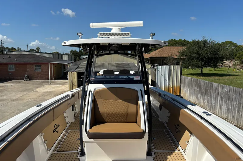 Slide: The Image of 2019 Fountain 38 CC LS boat with tan seating and deck, parked near a house. - 10