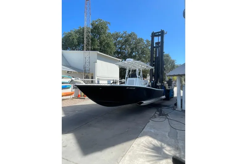 The Image of 2015 Barker Boatworks 26 Bay, black hull, docked near a metal building and palm trees. - 0