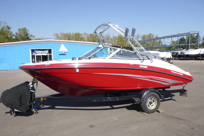 The Image of 2015 Yamaha Boats SX192 in red, parked on a trailer outside a showroom. - 1