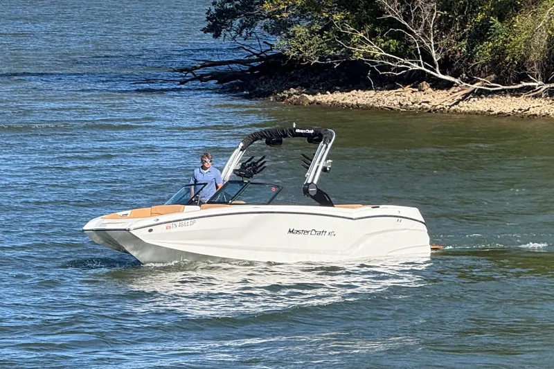 Slide: The Image of 2022 MasterCraft NXT24 boat cruising on a lake near a wooded shoreline. - 21