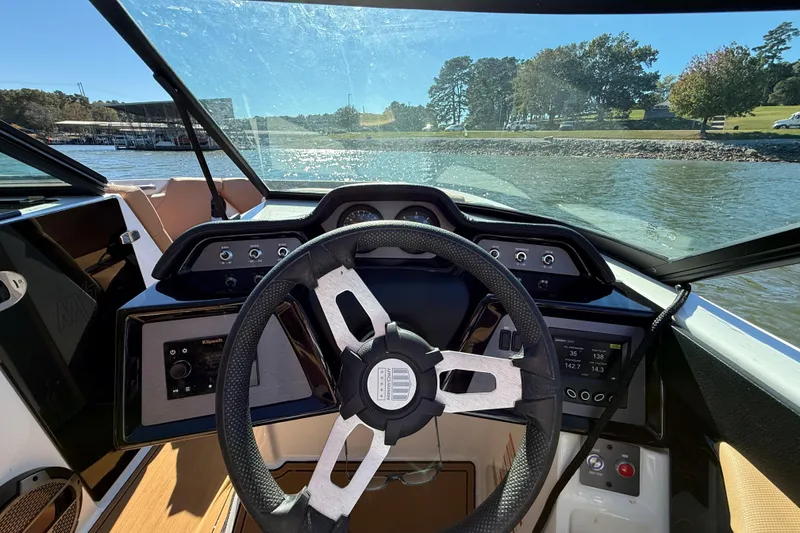 Slide: The Image of 2022 MasterCraft NXT24 boat dashboard with steering wheel, on a sunny day by the lake. - 42