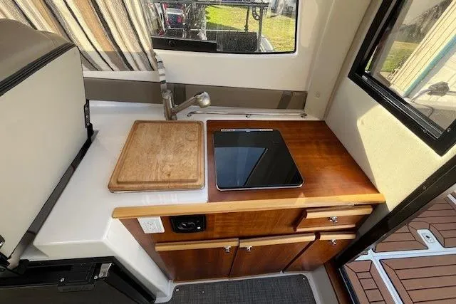 Slide: The Image of 2020 Cutwater C-24 Coupe kitchen area with stove, sink, and wooden cabinetry. - 24