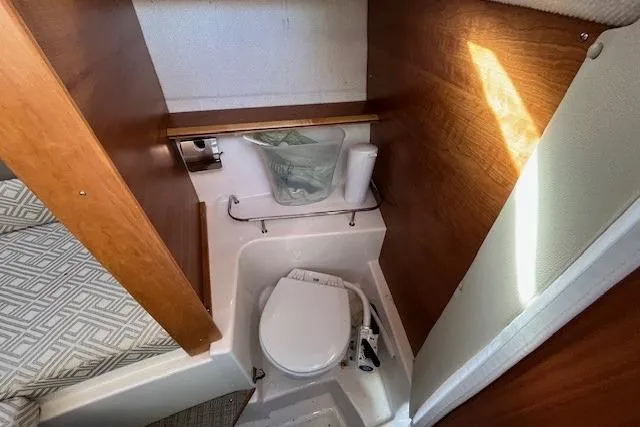 Slide: The Image of 2020 Cutwater C-24 Coupe boat interior bathroom with compact toilet and wooden accents. - 26