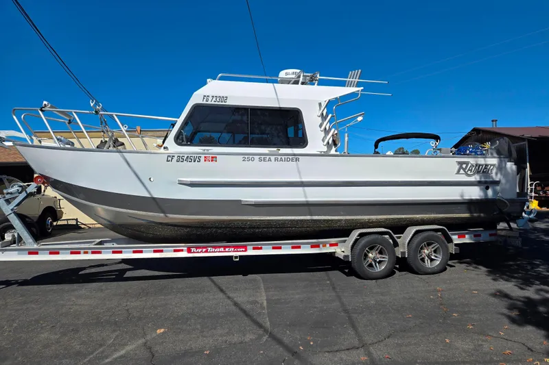 Slide: The Image of 2020 Raider 250 Sea Raider boat on trailer, parked outdoors under clear blue sky. - 1