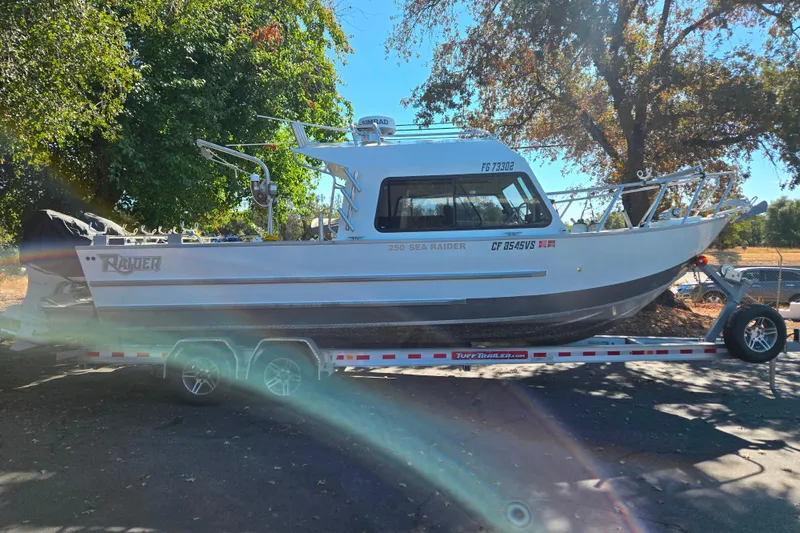 Slide: The Image of 2020 Raider 250 Sea Raider boat on trailer, parked outdoors under trees. - 2