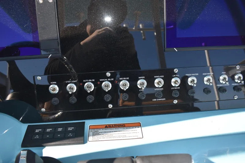 Slide: The Image of Control panel of 2025 NauticStar 332 Offshore boat with various switches and warning label. - 53