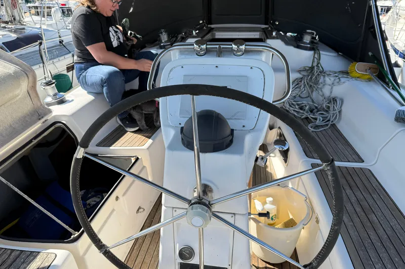 Slide: The Image of Steering wheel of a 2002 Bavaria 37 Sloop sailboat with a person seated nearby. - 4