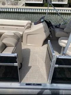 Slide: The Image of 2022 Avalon Catalina Entertainer 24' boat interior with beige seating and helm, docked by water. - 18