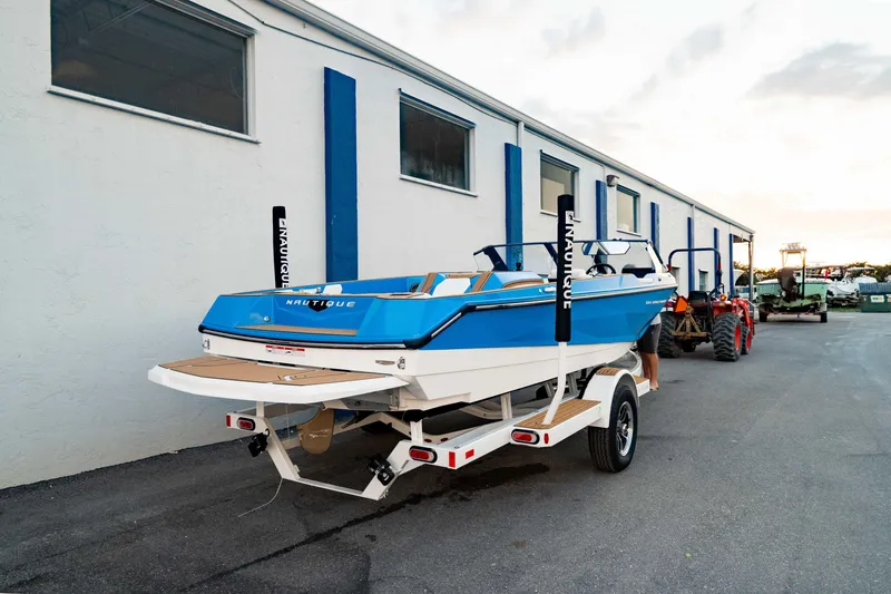 Slide: The Image of 2026 Nautique Ski Nautique boat on trailer, parked beside a building at sunset. - 10