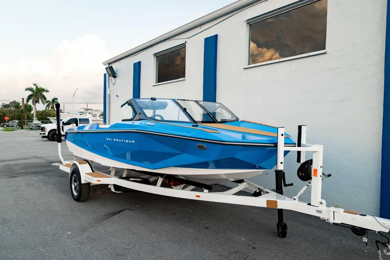 Slide: The Image of 2026 Nautique Ski Nautique boat in blue on a trailer, parked outside a building. - 9