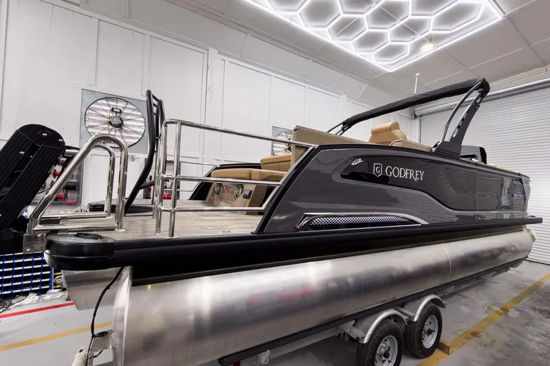 Slide: The Image of 2026 Godfrey Sanpan 25' Tritoon boat in a showroom, featuring sleek design and modern amenities. - 10