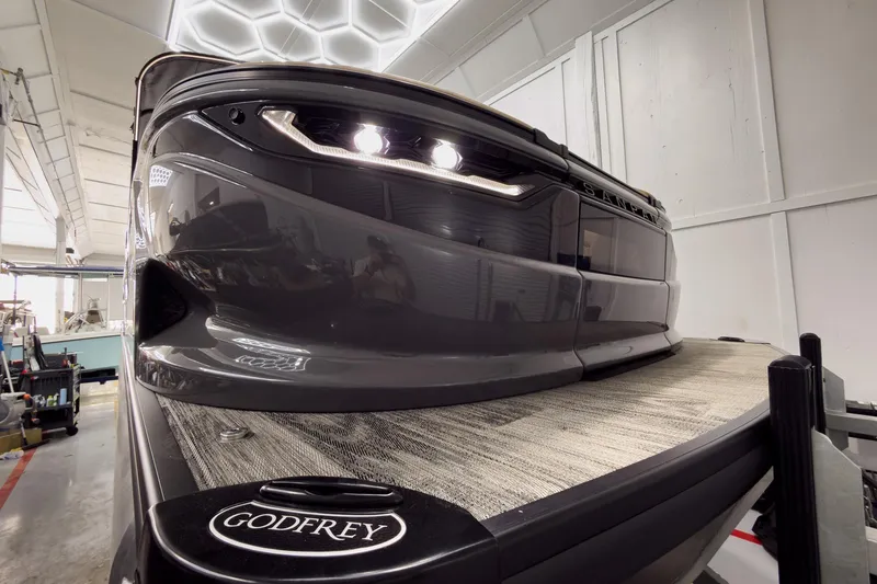 Slide: The Image of 2026 Godfrey Sanpan 25' Tritoon boat in showroom, showcasing sleek design and lighting. - 2