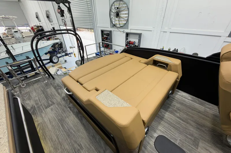 Slide: The Image of 2026 Godfrey Sanpan 25' Tritoon with tan flip lounge in a workshop setting. - 36