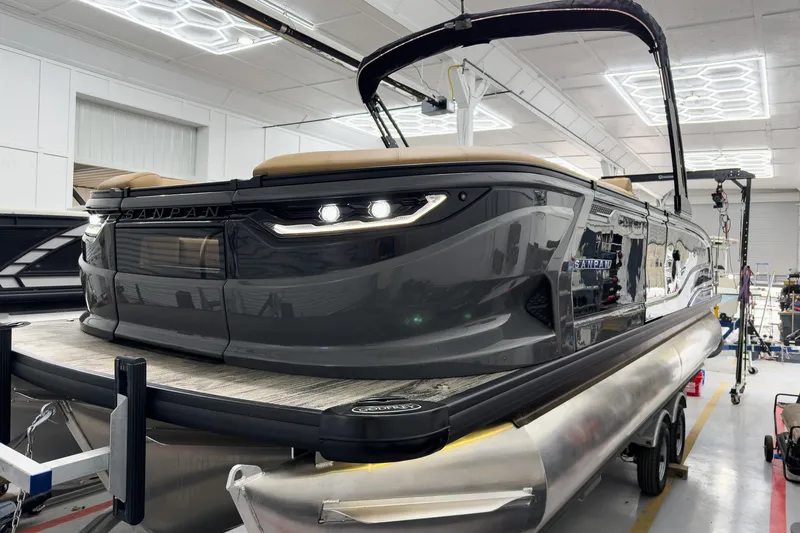 Slide: The Image of 2026 Godfrey Sanpan 25' Tritoon boat in showroom, featuring sleek design and modern lighting. - 5