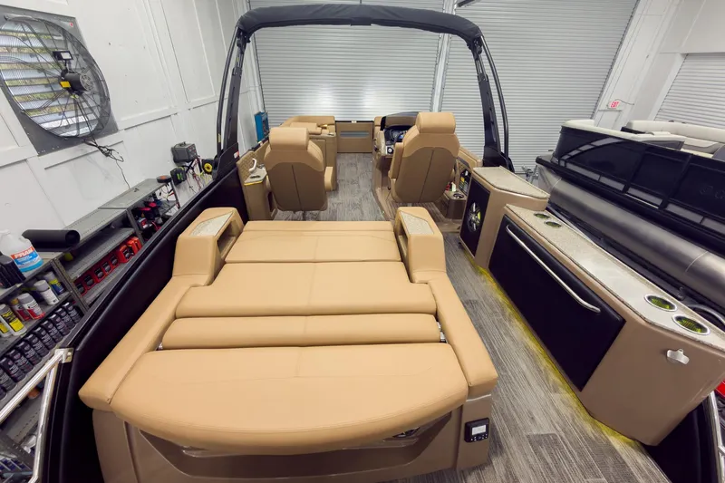 Slide: The Image of 2026 Godfrey Sanpan 25' Tritoon with luxurious tan seating and modern amenities in a showroom. - 50